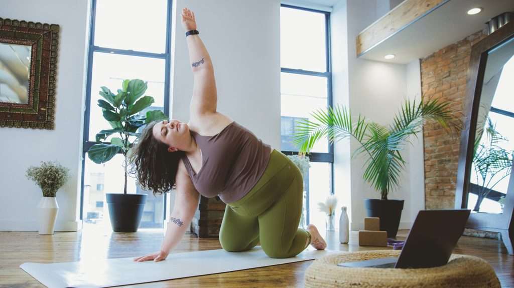 Image of plus size female on yoga mat stretching one arm up to the sky working on their flexibility training