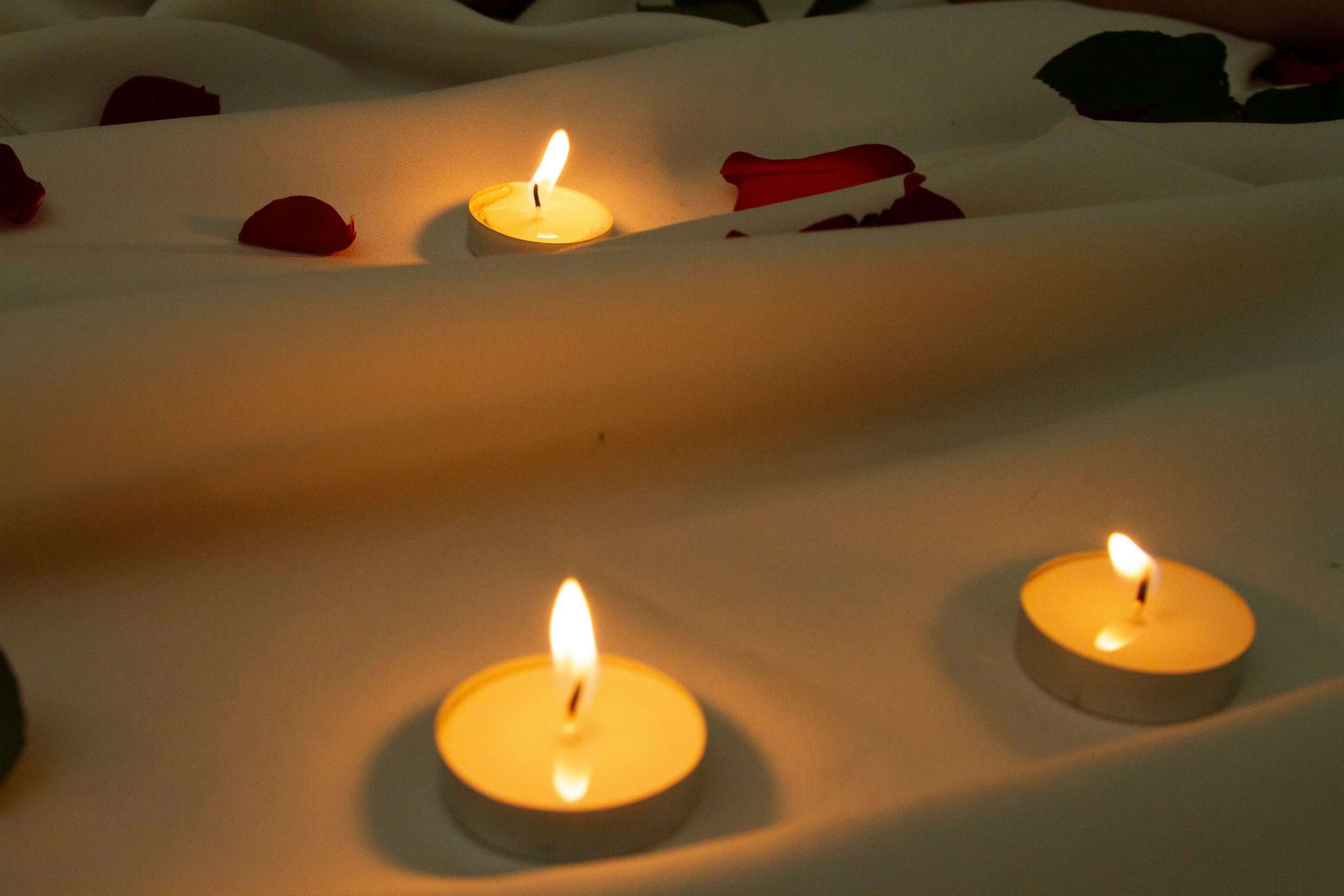 image of candles near rose petals on bed sheet
