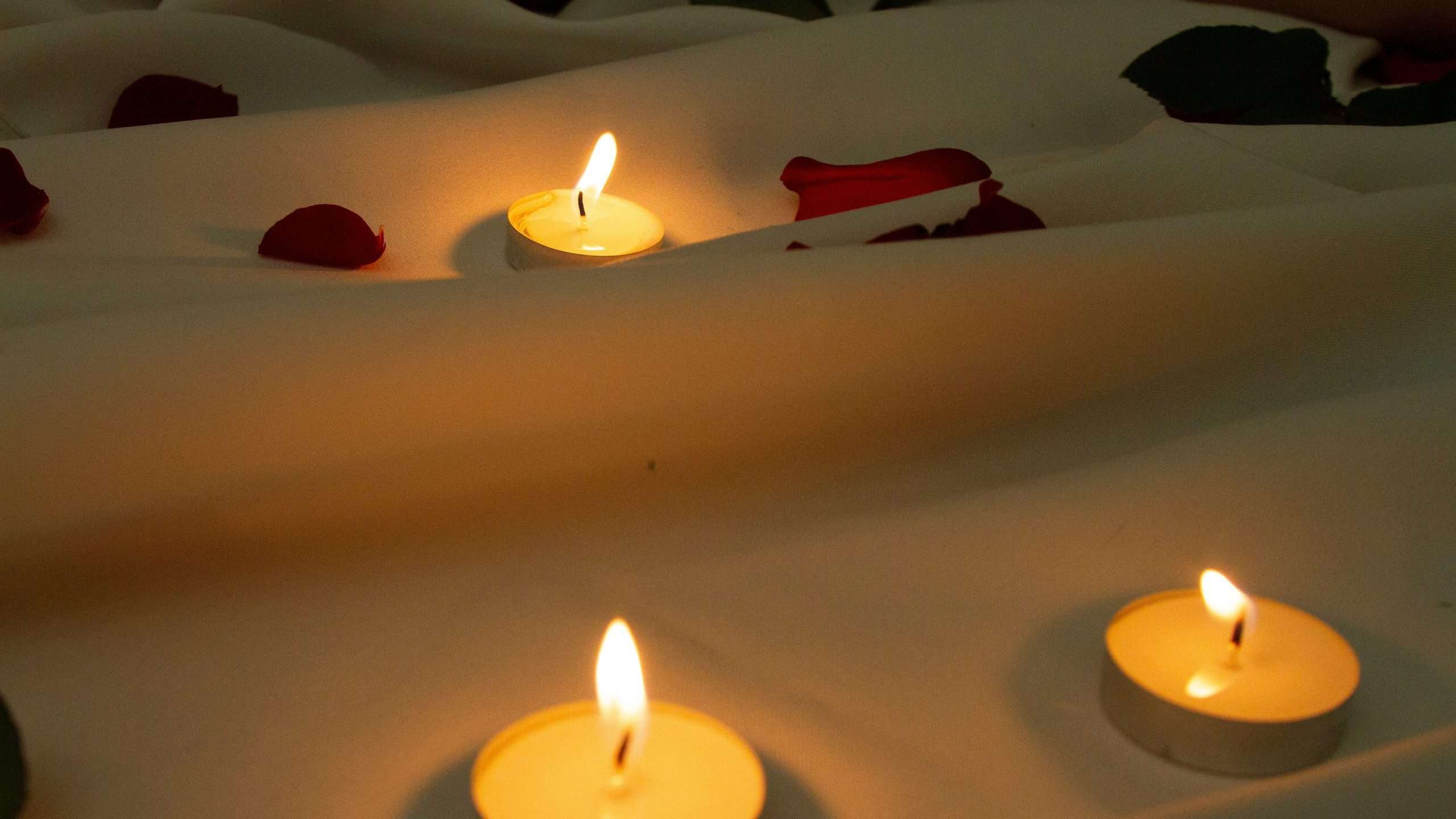 image of candles near rose petals on bed sheet