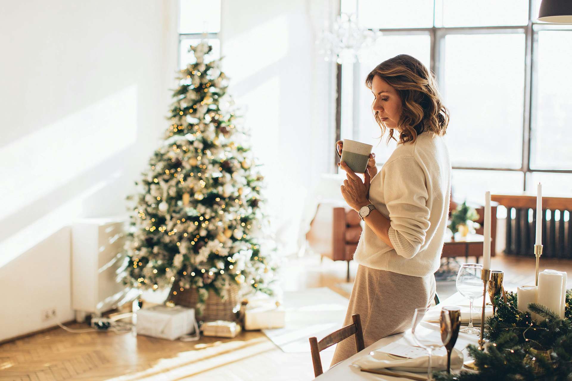 Person looking down in front of christmas tree managing holiday stress with self-care and tea