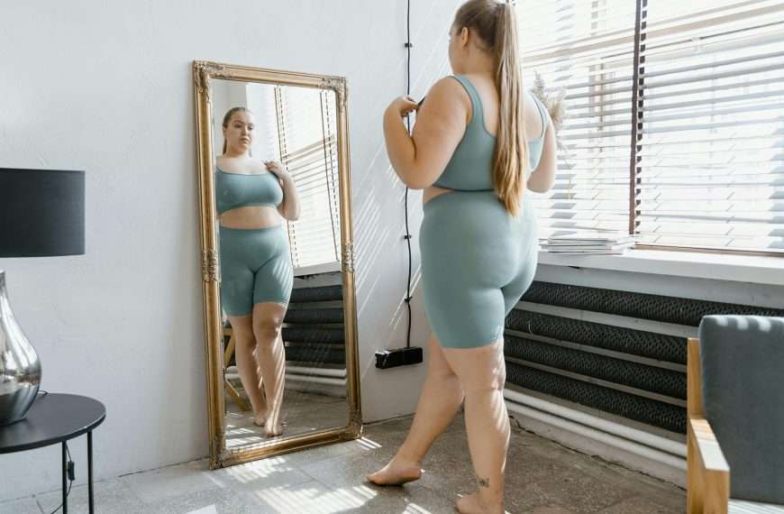 mid-size woman in activewear looking at self in mirror as an example of body grief
